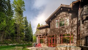 A two-story wooden cabin with large windows and a stone patio.