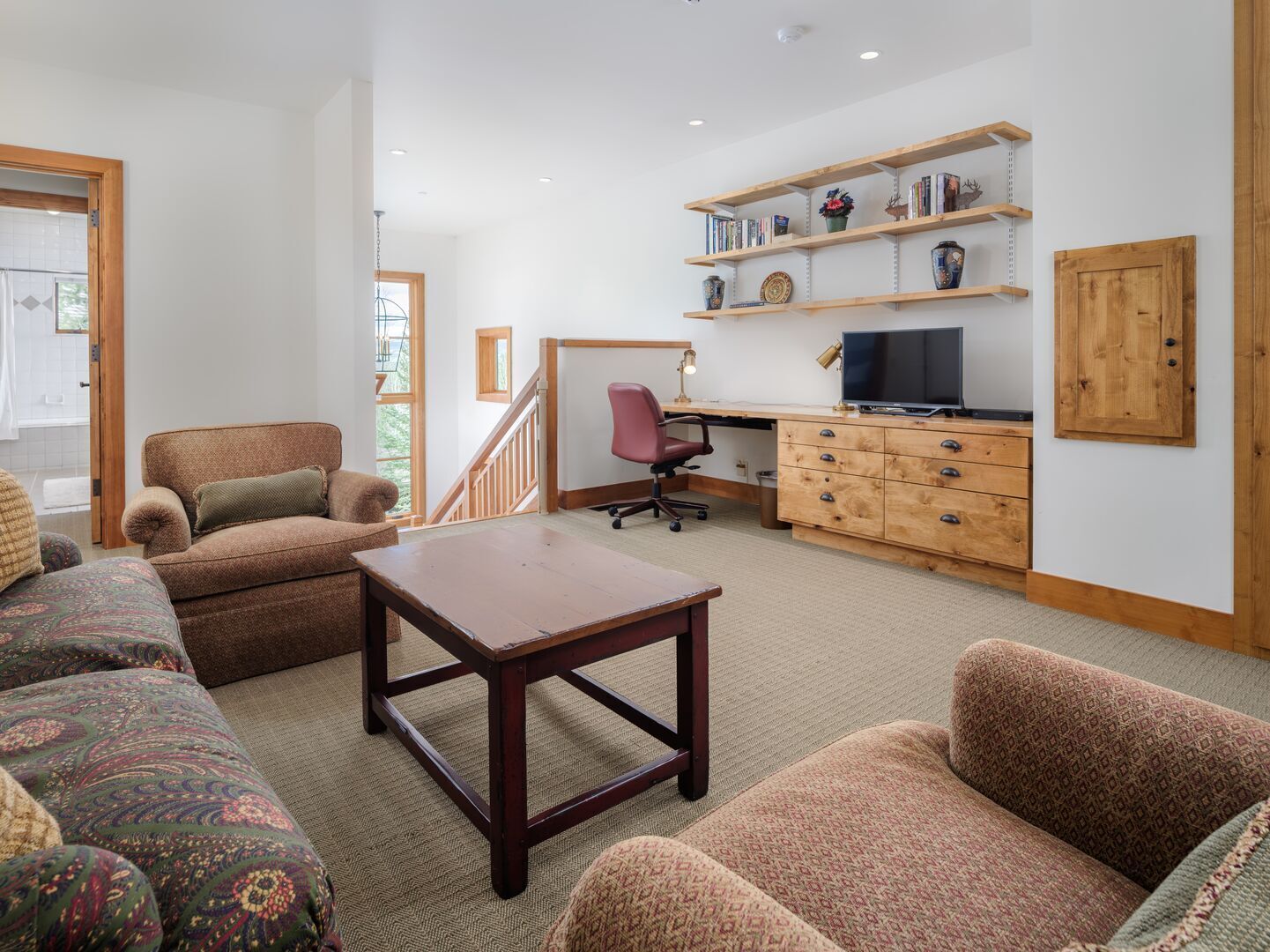 A spacious living room with a wooden desk, a comfortable sofa, and a television.