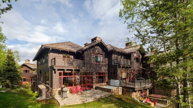 A large, multi-story wooden house with a balcony, a patio with outdoor seating, and a stone pathway.