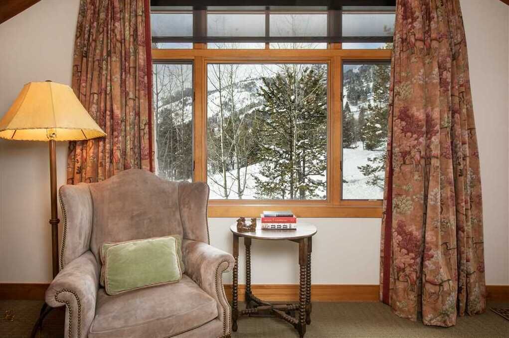 A cozy room with a large window, a plush armchair, a small table, and a lamp.