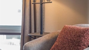 Een kamer met een grijze bank, een rood kussen, een lamp met een bosmotief en een prent van een wolf aan de muur.