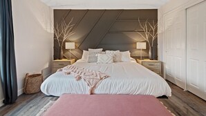 A bedroom with a large bed, two bedside tables, a bench, and a ceiling with a sloped design.