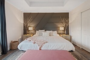 A bedroom with a large bed, two bedside tables, a bench, and a ceiling with a sloped design.