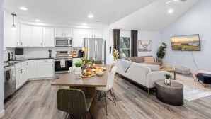 A modern kitchen with white cabinets, stainless steel appliances, and a dining area with a wooden table and chairs.