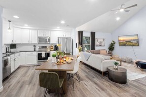 Eine moderne Küche mit weißen Schränken, Edelstahlgeräten und einem Essbereich mit Holztisch und Stühlen.