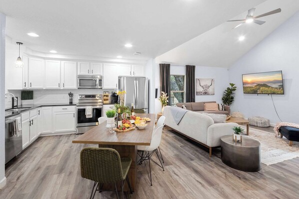 A modern kitchen with white cabinets, stainless steel appliances, and a dining area with a wooden table and chairs.
