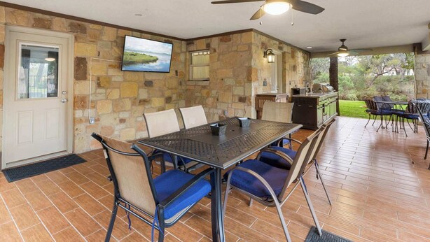 An outdoor patio with a table and chairs, a ceiling fan, and a stone wall.