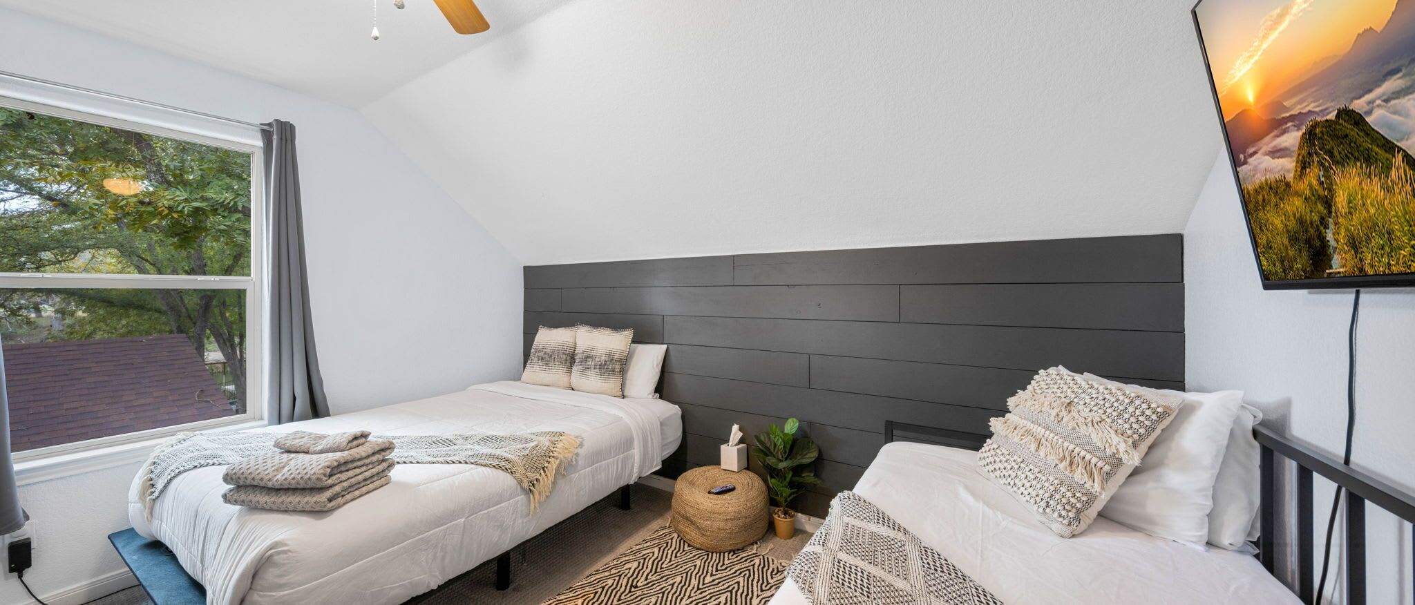 Un dormitorio moderno con dos camas, un ventanal grande y un televisor montado en la pared.