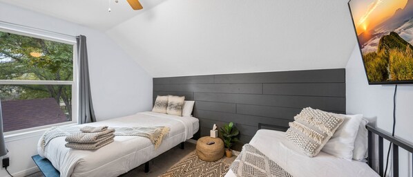 Un dormitorio moderno con dos camas, un ventanal grande y un televisor montado en la pared.