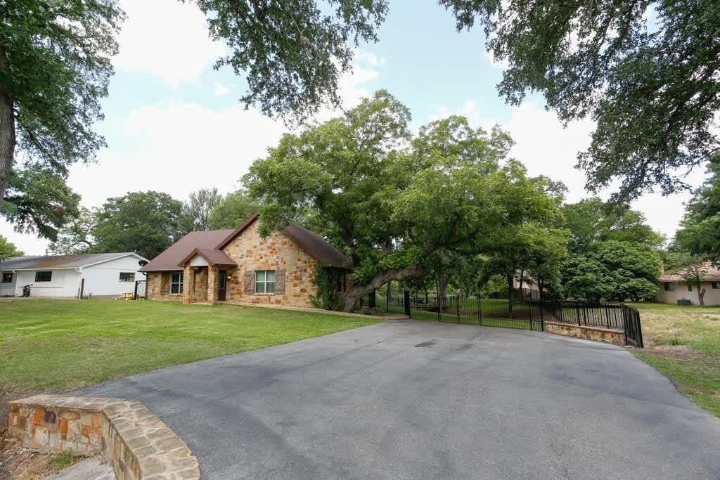 A stone house with a paved driveway and a black metal fence.