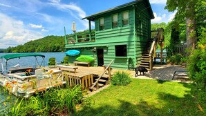 Une cabane en bois peinte en vert, avec un quai, un bateau et une zone herbeuse.