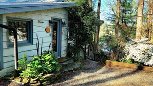 Une maison avec un chemin de gravier menant à une porte en bois, entourée de verdure et d’arbres.