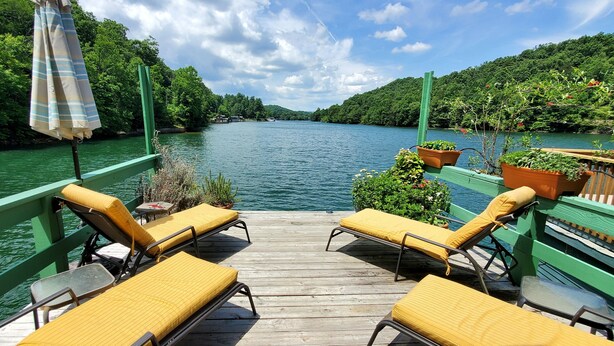 Une terrasse en bois avec des chaises rembourrées jaunes et une balustrade verte, donnant sur une rivière paisible.