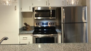 A kitchen with white cabinets, a stainless steel stove, a microwave, and a refrigerator. There are two pendant lights hanging from the ceiling. - Horizons single story ground floor 2 bdrm (Mammoth Lakes)