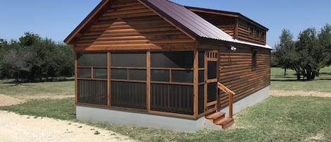A wooden cabin with a large window, a porch, and a metal roof.