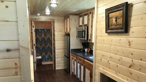 Interior de una cabaña de madera con zona de cocina, que incluye armarios, un refrigerador y un microondas.