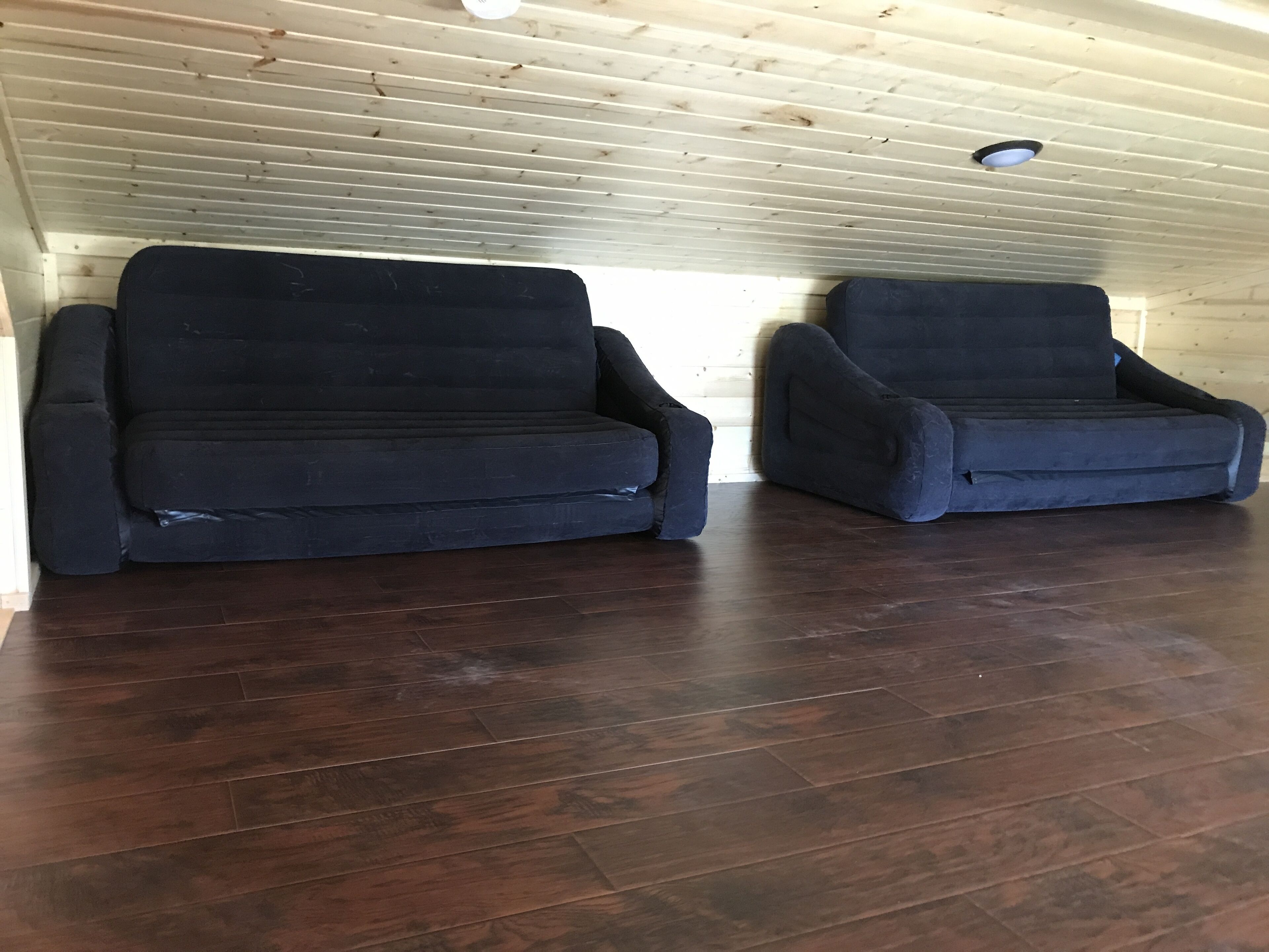 Ein Raum mit Holzboden und schrägen Wänden, ausgestattet mit zwei dunkelgrauen Sofas.
