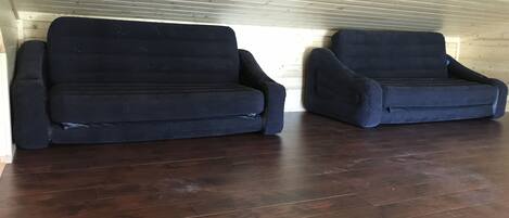 Ein Raum mit Holzboden und schrägen Wänden, ausgestattet mit zwei dunkelgrauen Sofas.
