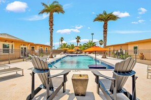 A pool area with lounge chairs, umbrellas, and palm trees.
