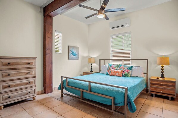 A bedroom with a bed, wooden dresser, nightstands, lamps, a ceiling fan, and a window with blinds.