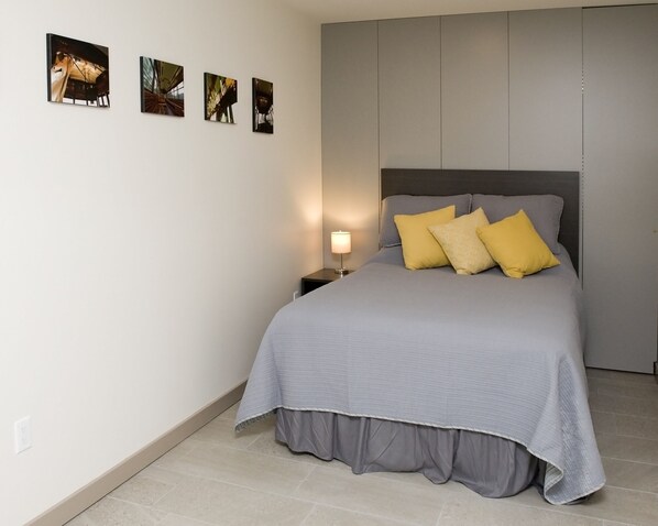 A bedroom with a bed, a nightstand, a lamp, and four framed pictures on the wall.