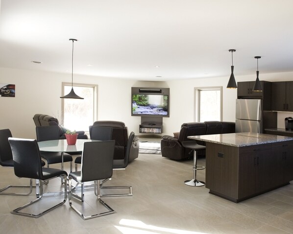 A modern kitchen with a central island, dining area with chairs, and a TV mounted on the wall.