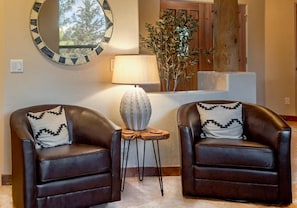 Deux fauteuils en cuir avec des coussins à motifs, un miroir rond, une lampe et une plante dans un salon.