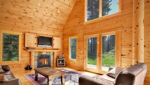 A cozy cabin interior with a fireplace, leather sofas, and large windows offering a view of the forest.