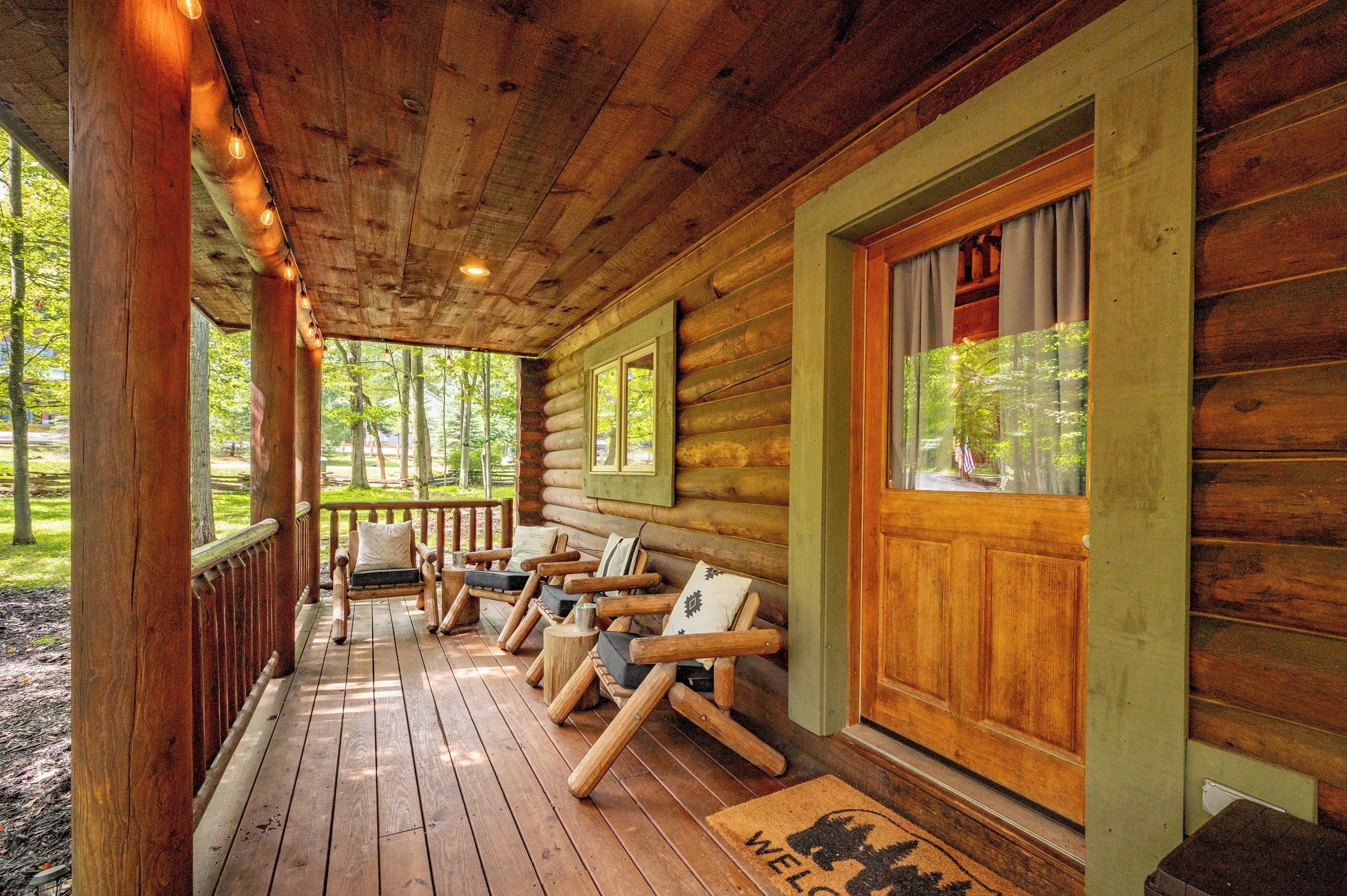 A log cabin with a porch, wooden furniture, and a welcome mat.