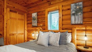 Ein Schlafzimmer in einer Holzhütte mit einem Bett, Kissen, einem Fenster und Wandleuchten.