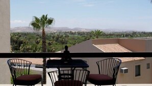 A balcony with a table and chairs, overlooking a landscape with palm trees and distant mountains. - Beautiful Remodeled Condo near DownTown and Beach in San Jose del Cabo. (San Jose del Cabo,B.C.S.23406)
