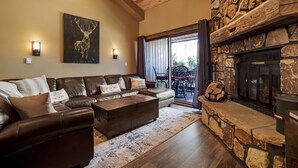 A cozy living room with a stone fireplace, leather sofa, and a large painting on the wall.