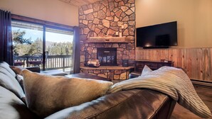 A cozy living room with a stone fireplace, leather sofa, and a flat-screen TV mounted on the wall.