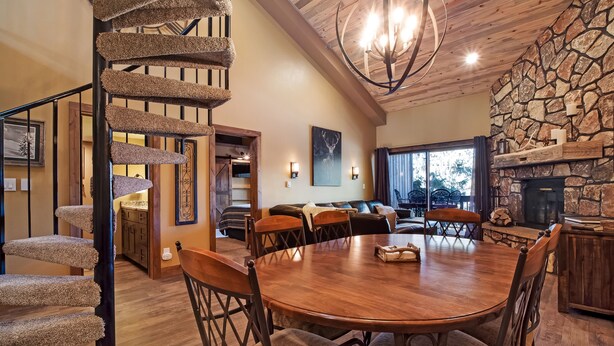 A spacious dining area with a wooden table and chairs, a spiral staircase, and a stone fireplace.
