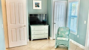 Quarto com cama, cômoda, cadeira e televisão.