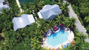 Une vue aérienne d’un complexe hôtelier doté d’une piscine entourée de palmiers et de quelques bâtiments.