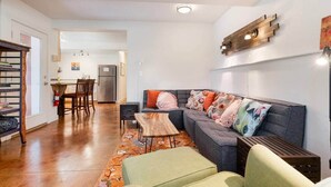 A living room with a sofa, a coffee table, and a rug. There is a kitchen in the background with a refrigerator and a dining table. - Walkable Sellwood 2BR Apartment (Portland)