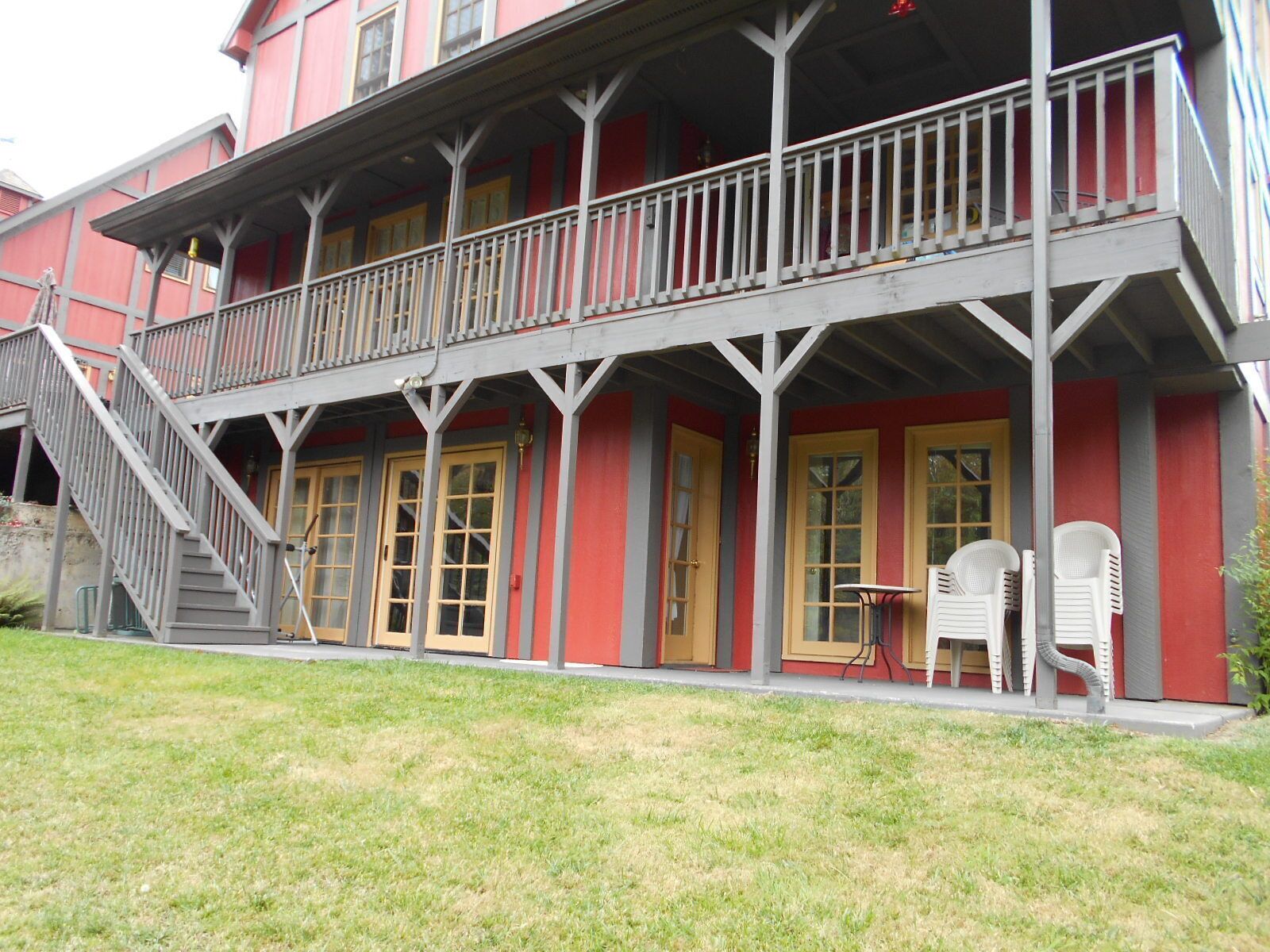 Un bâtiment à deux étages doté d’un balcon, d’un escalier et d’un petit espace extérieur aménagé avec des chaises.