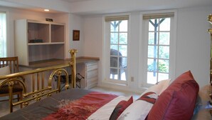 Une chambre à coucher avec un lit, un bureau et une chaise. Il y a deux fenêtres donnant sur des arbres.