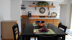 Un coin repas comprenant une table en bois, des chaises, une machine à café, une horloge et une étagère avec des objets décoratifs.