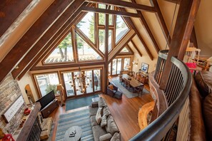 A spacious loft-style living area with a high ceiling, large windows, and a fireplace. - Architectural Gem w/ Dock & Dock Slip (Swanton)
