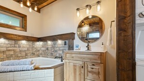 A bathroom with a stone wall, a wooden vanity, a round mirror, and a bathtub. - Canyon View Treehouse- Summer Vacation With A View (Jasper)