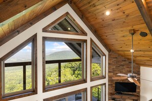 A room with large windows offering a view of a forested mountain range.