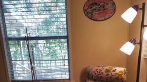 Een stoel met bloemenstof, een klein krukje en een vloerlamp in een kamer met een raam en een bord aan de muur.