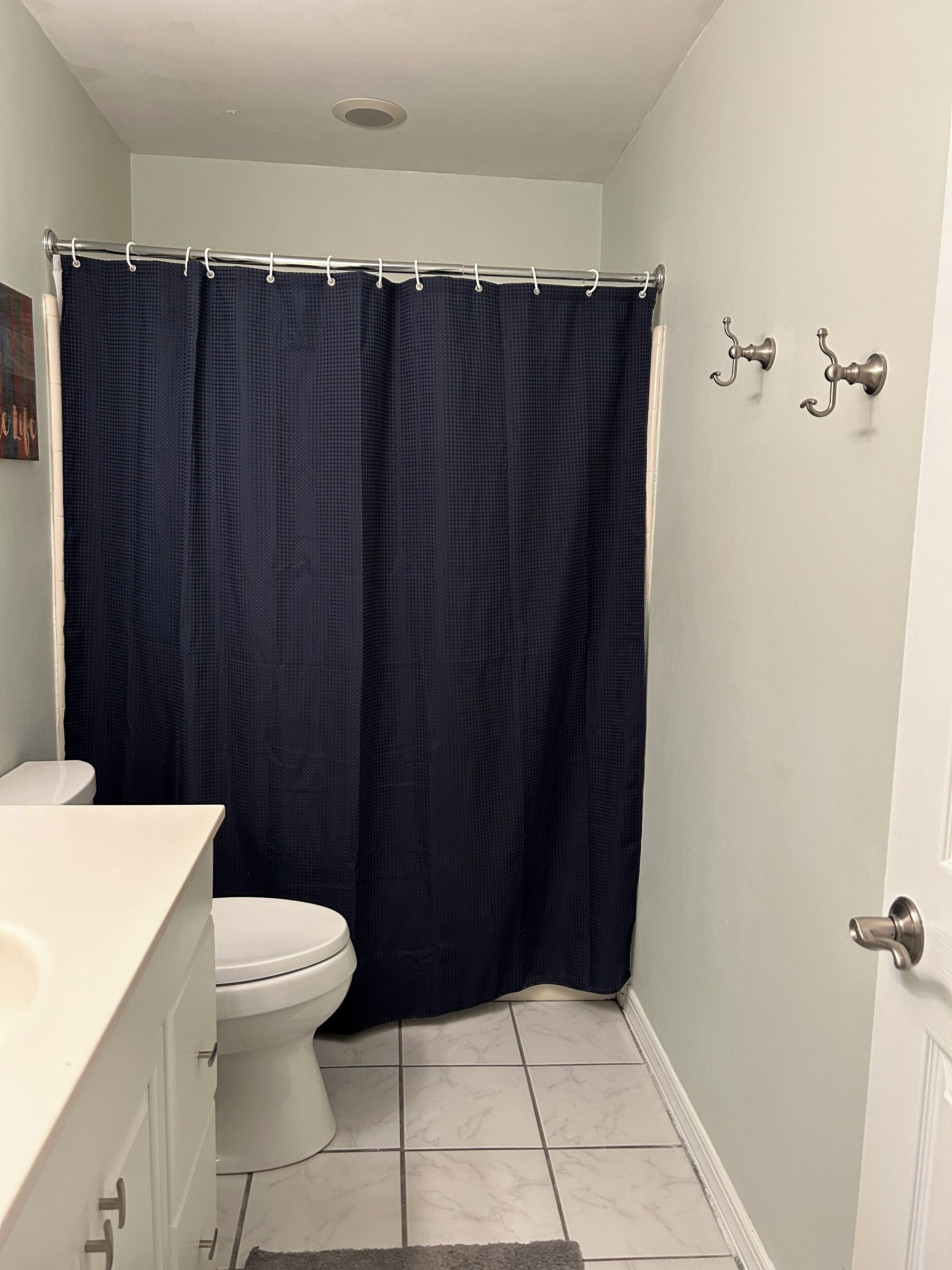 Un baño con inodoro blanco, lavamanos blanco y cortina de ducha azul oscuro.