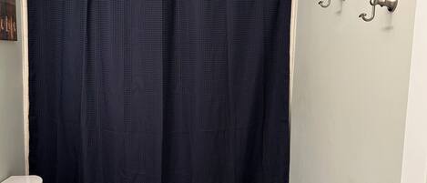 Un baño con inodoro blanco, lavamanos blanco y cortina de ducha azul oscuro.