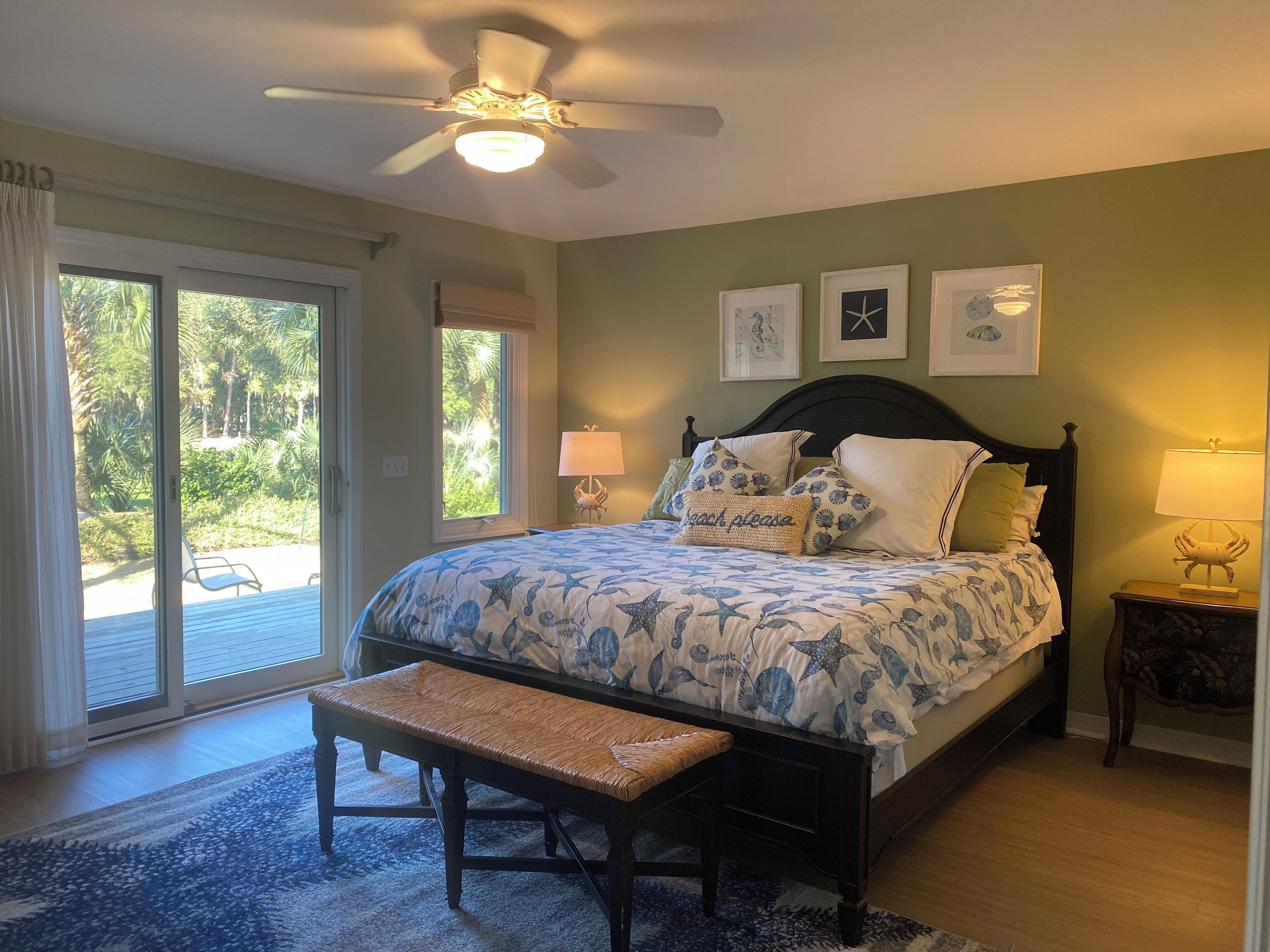 Une chambre à coucher comprenant un lit, un banc, un ventilateur de plafond et une vue sur un jardin, accessible par une porte coulissante.