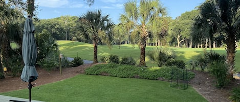 Un patio con dos sillas y una mesa, con vistas a un césped cuidado y un campo de golf.