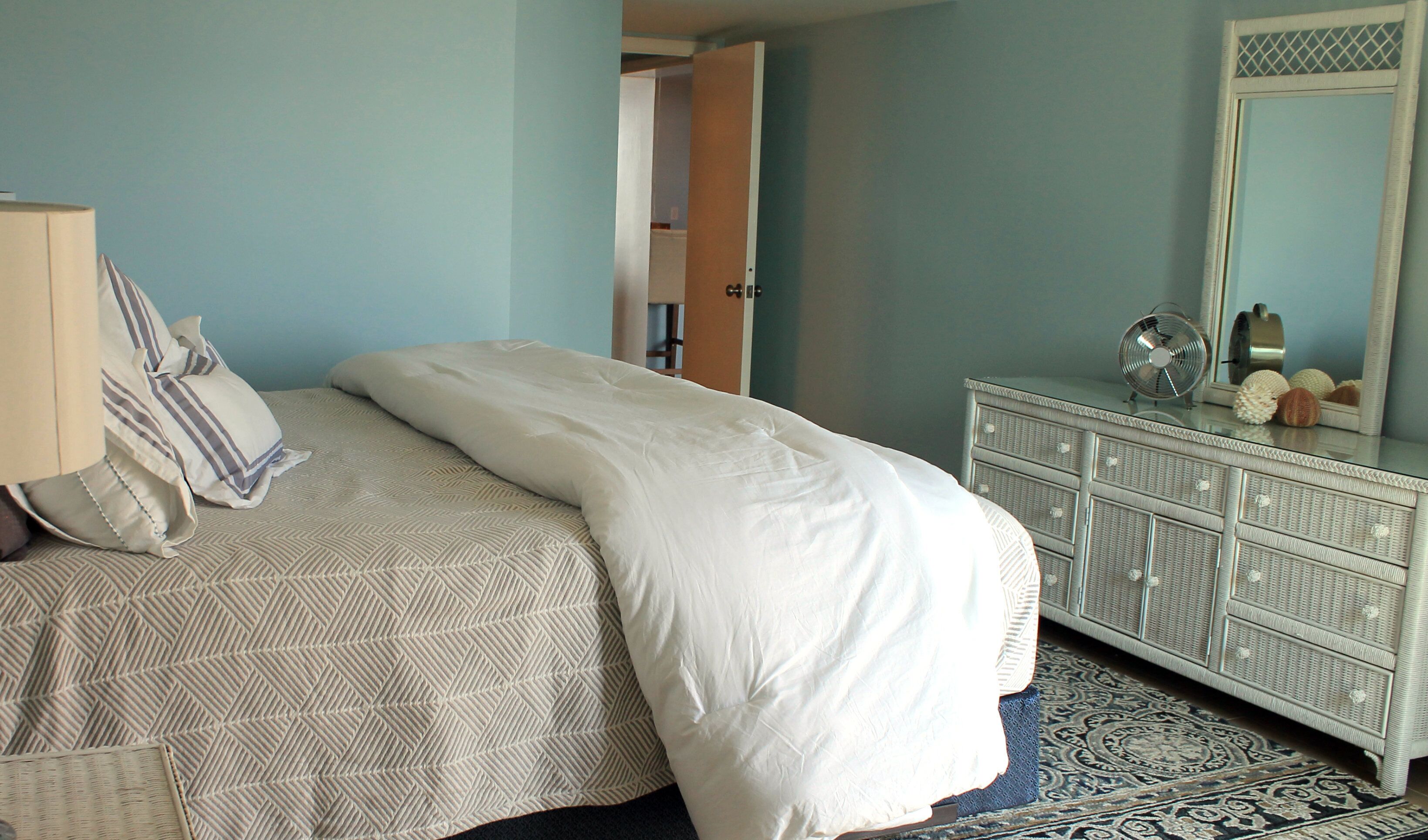 Un dormitorio con cama, cómoda, espejo y una alfombra estampada.