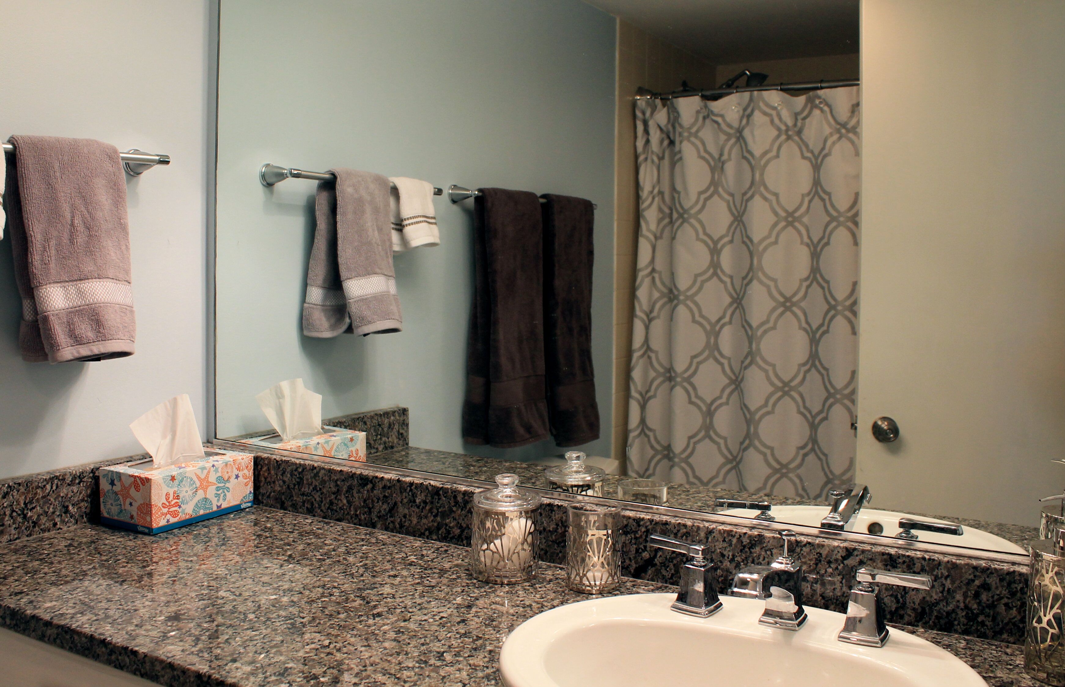 A bathroom with a granite countertop, a sink, a mirror, and a shower curtain.